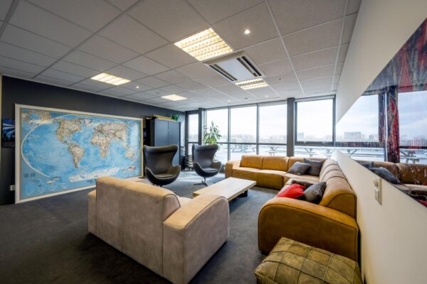 Loungehoek in een modern kantoor aan de Anthony Fokkerweg met comfortabele banken, een wereldkaart aan de muur en uitzicht op een terras.